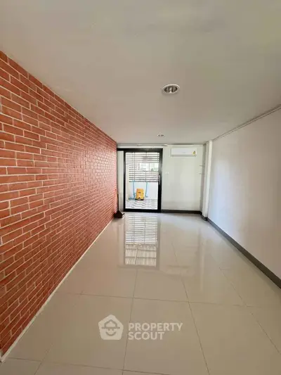 Spacious modern room with brick accent wall and large window for natural light.