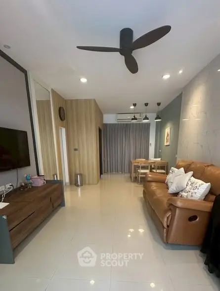 Modern living room with ceiling fan, leather sofa, and dining area in open layout.