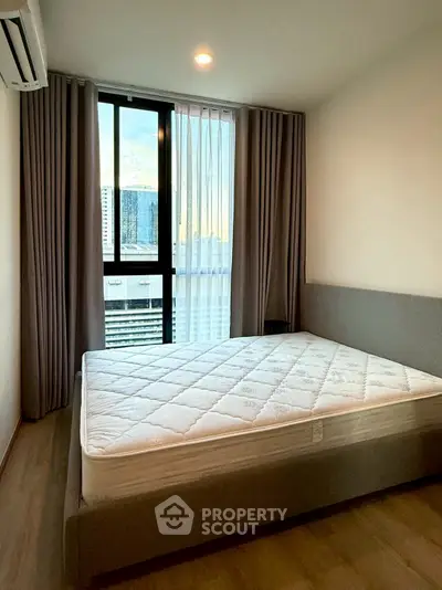Modern bedroom with large window and city view, featuring a comfortable bed and elegant curtains.