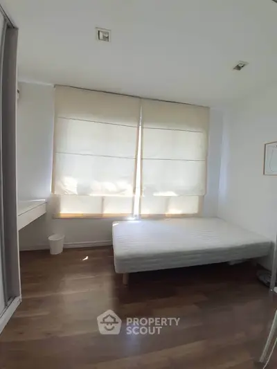 Bright minimalist bedroom with wooden flooring and large window shades.