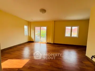 Spacious sunlit room with wooden flooring and large windows in a modern home.