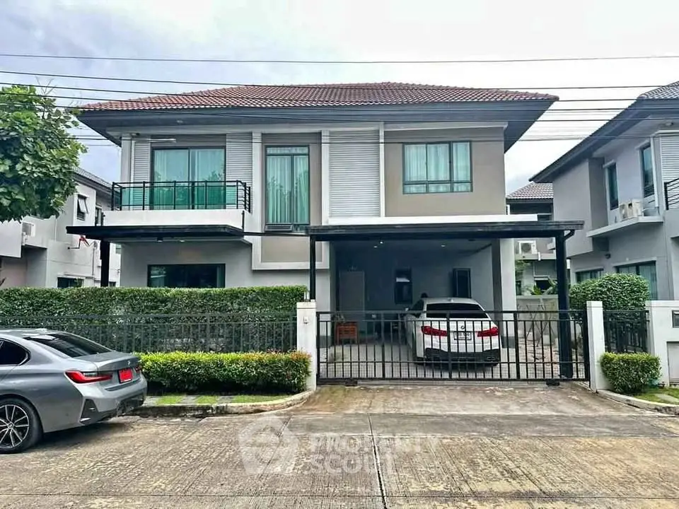 Modern two-story house with gated driveway and lush greenery in suburban setting.