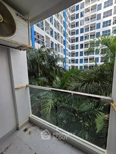 Modern balcony with glass railing overlooking lush greenery and contemporary building facade.