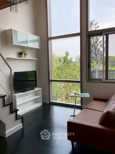 Modern living room with high ceilings and large windows offering lush garden views.