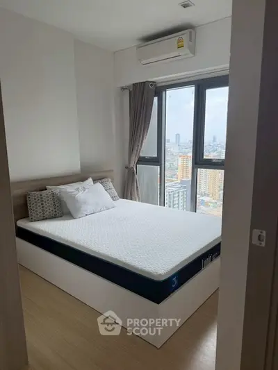 Modern bedroom with city view, featuring a comfortable bed and large windows for natural light.