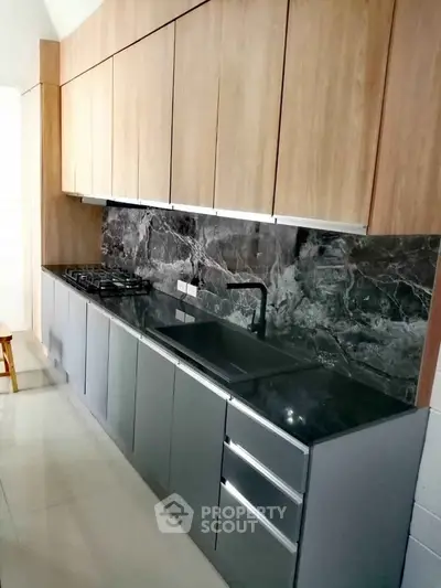 Modern kitchen with sleek cabinetry and marble backsplash, featuring a gas stove and ample storage space.