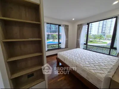 Spacious bedroom with large windows offering a stunning view of modern high-rise buildings and a pool.