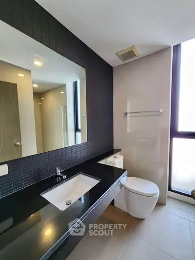Modern bathroom with sleek black countertop and large mirror in a contemporary apartment.