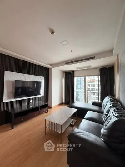 Modern living room with sleek black sofa and large TV, featuring floor-to-ceiling windows with city view.