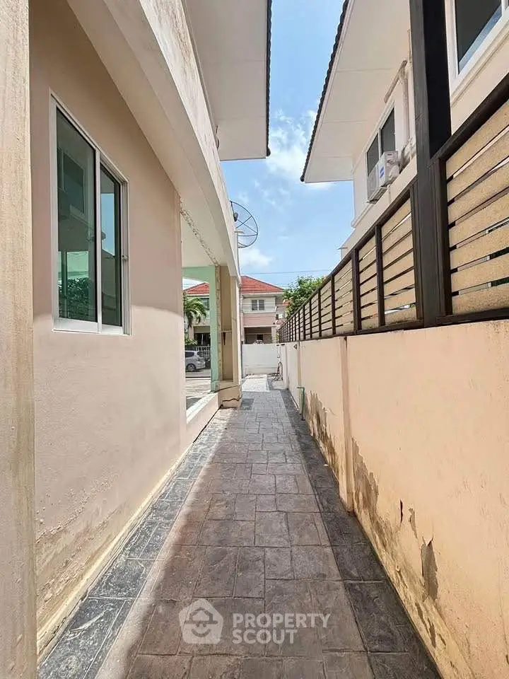 Narrow exterior walkway between modern houses with tiled pathway and clear sky view.
