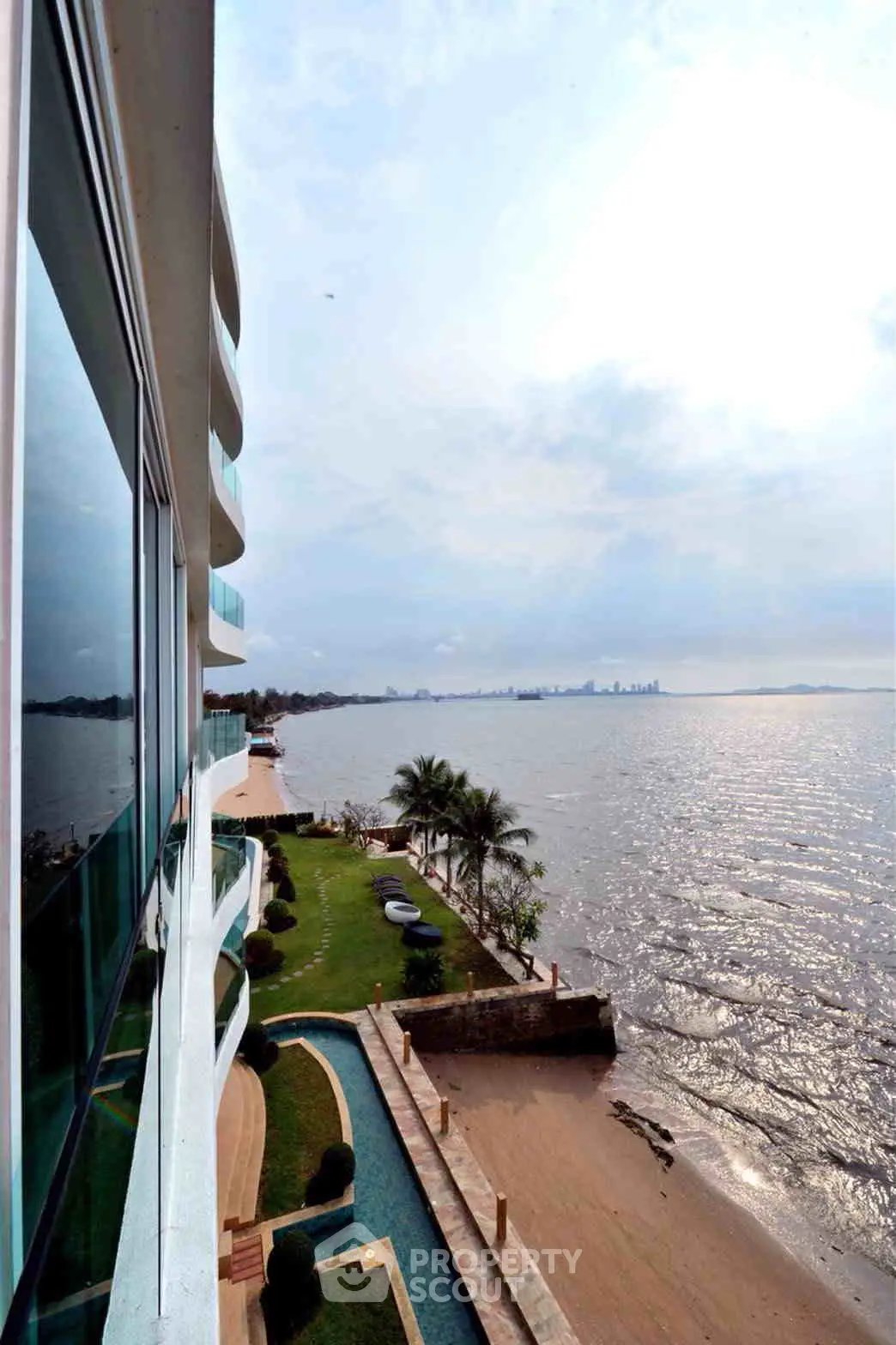 Stunning waterfront view from modern apartment building with lush garden and city skyline in the distance.