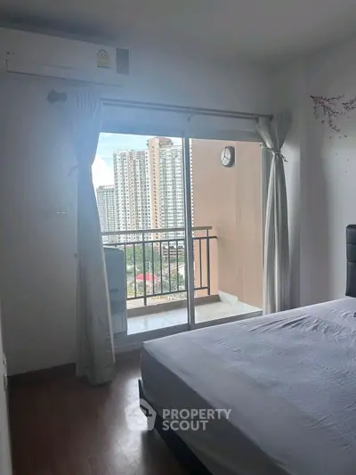 Modern bedroom with balcony view of city skyline, featuring large windows and natural light.