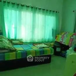 Cozy bedroom with colorful bedding and large window with green curtains.