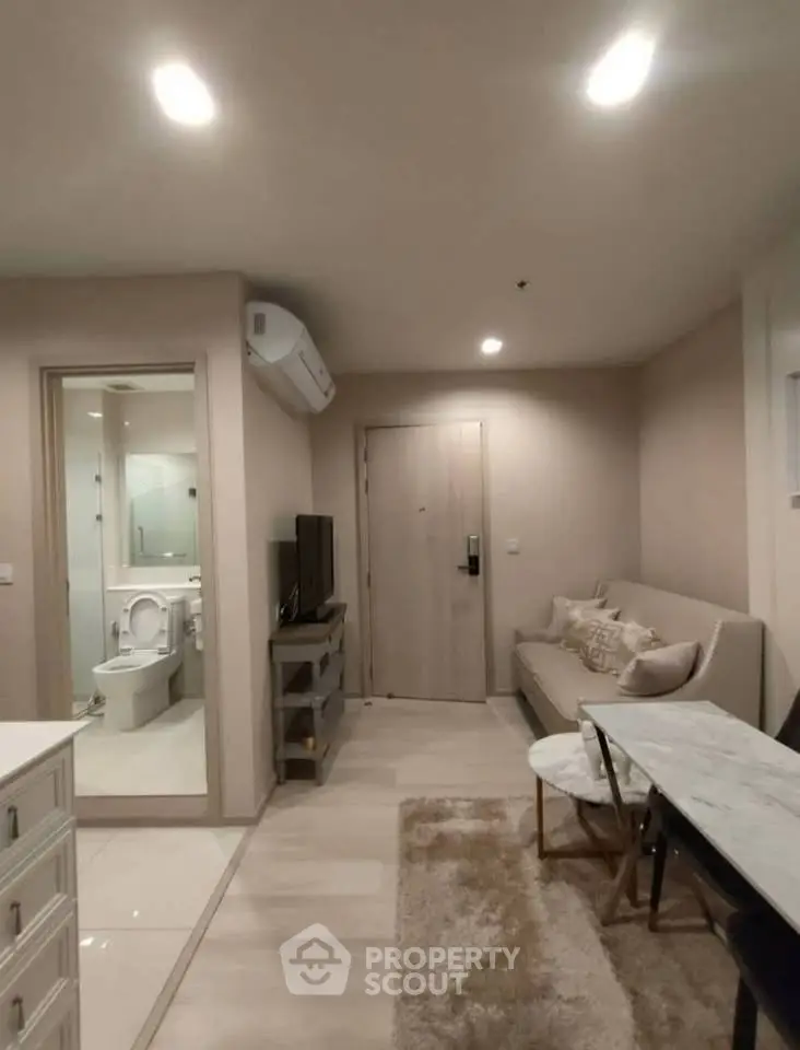 Modern living room with open view to bathroom, featuring sleek furniture and neutral tones.