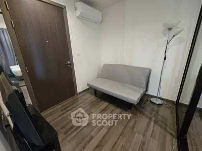 Modern small living room with sofa and floor lamp, featuring wooden flooring and air conditioning.