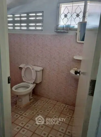 Cozy bathroom with pink tiles and window, featuring a toilet and small shelves.