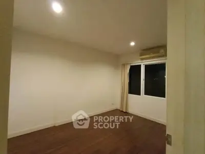 Spacious empty room with wooden flooring and large window, ideal for customization.