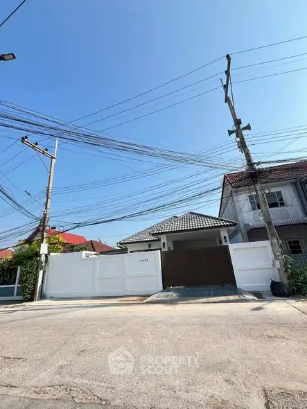 Charming suburban house with white fence and tiled roof under clear blue sky.