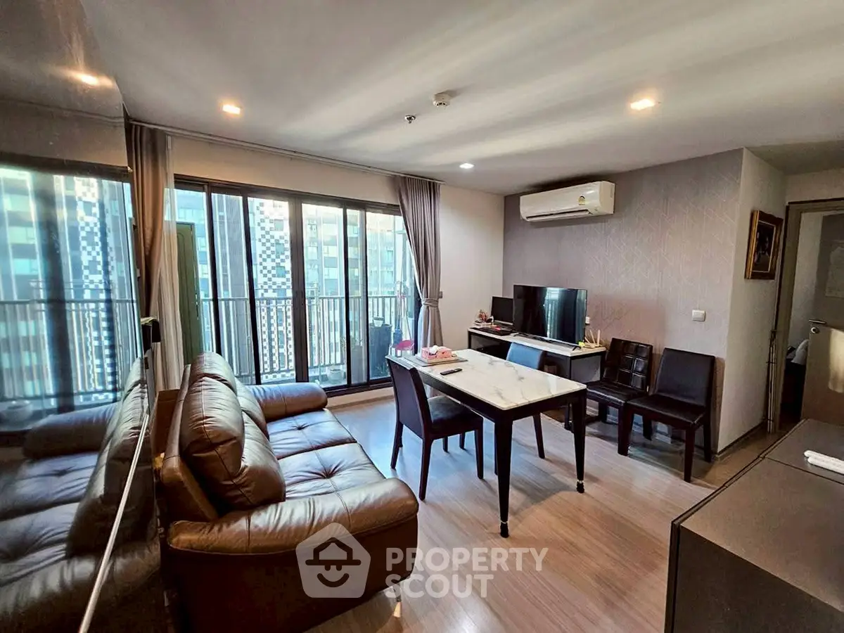 Modern living room with leather sofa, dining table, and city view balcony in high-rise apartment.