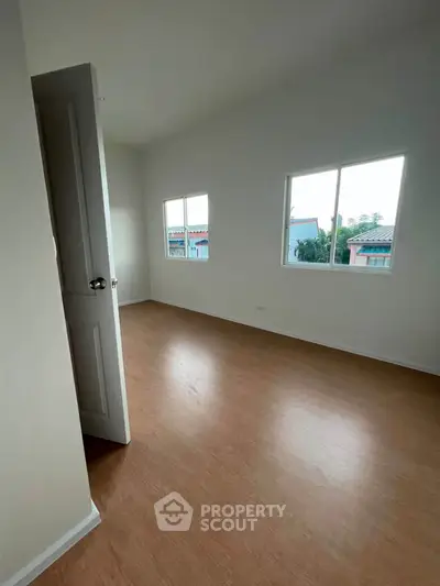 Spacious empty room with wooden flooring and large windows offering natural light and neighborhood views.
