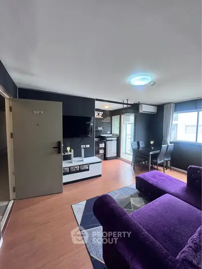 Modern living room with purple sofa, flat-screen TV, and dining area in open layout apartment.