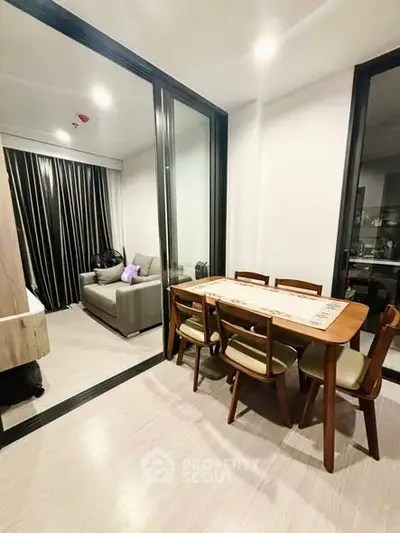 Modern dining area with wooden table and chairs adjacent to cozy living room in open-plan apartment.