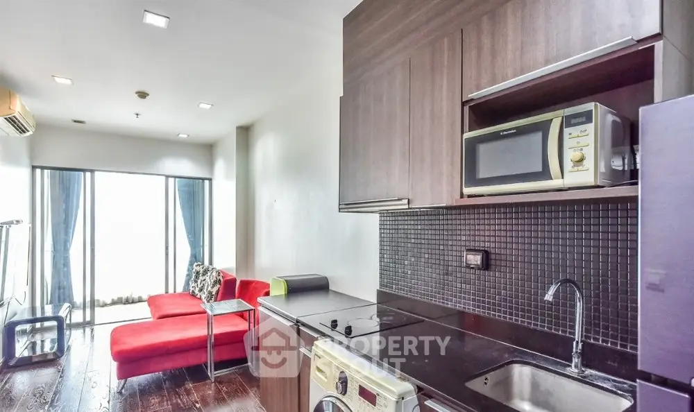 Modern apartment with sleek kitchen and cozy living area featuring red sofa and large windows.