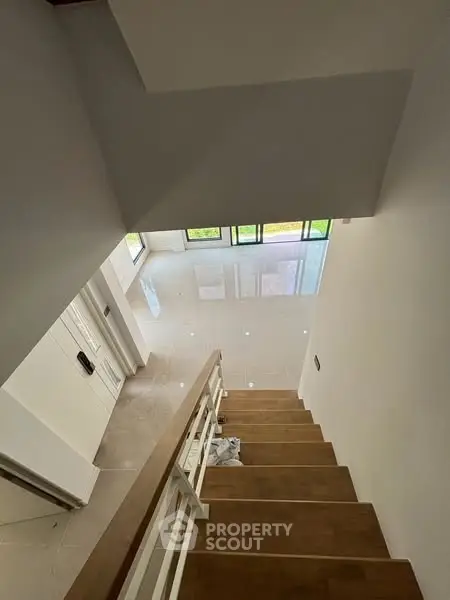 Modern staircase with polished floors and large windows in a bright home interior.