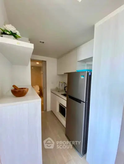 Modern compact kitchen with sleek appliances and minimalist design, featuring a stainless steel fridge and built-in microwave.