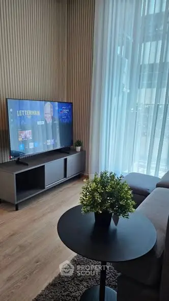 Modern living room with large TV, stylish furniture, and floor-to-ceiling windows offering natural light.