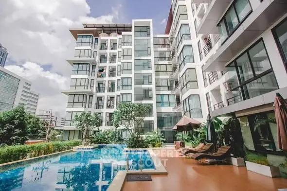 Modern apartment building with pool and lush greenery in urban setting.