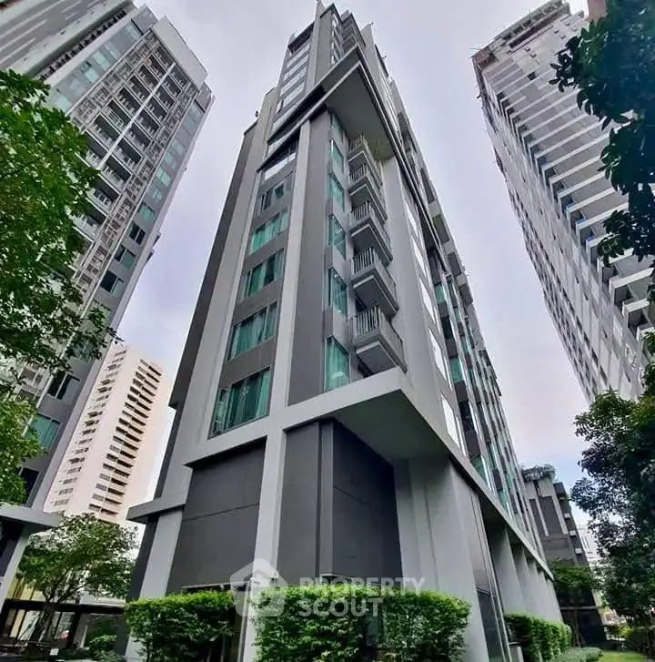 Modern high-rise building with sleek architecture and lush greenery in urban setting.