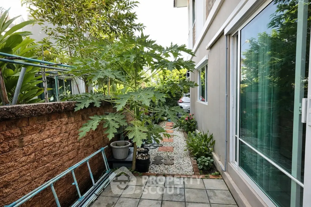 Charming garden pathway beside modern home with lush greenery and sliding glass doors.
