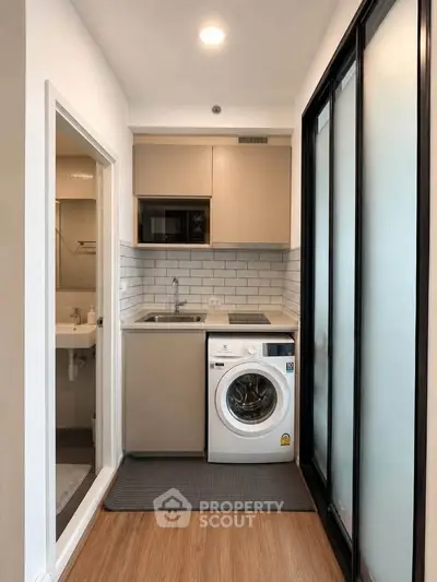 Compact kitchen with washing machine and microwave in modern apartment