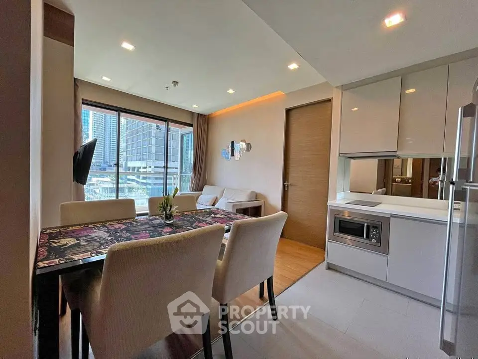 Modern open-layout living room with dining area and kitchen, featuring city views through large windows.