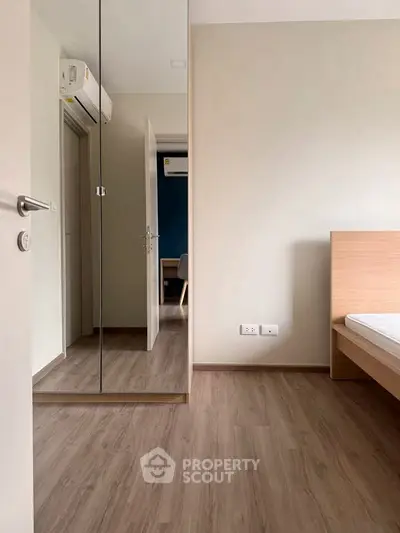 Modern minimalist bedroom with mirrored closet and wooden flooring.