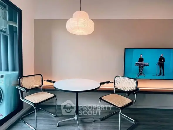 Modern living room with stylish chairs, round table, and TV, featuring sleek design and contemporary lighting.