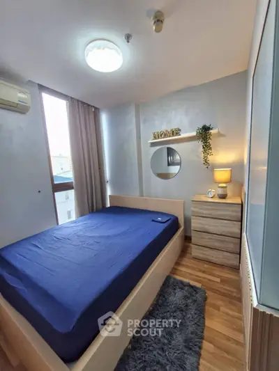 Cozy bedroom with modern decor, wooden flooring, and natural light from large window.