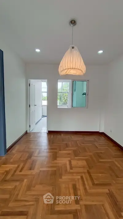 Spacious room with elegant parquet flooring and modern pendant light.