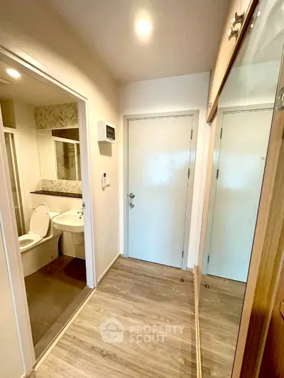 Modern apartment entrance with adjacent bathroom, featuring sleek design and wooden flooring.