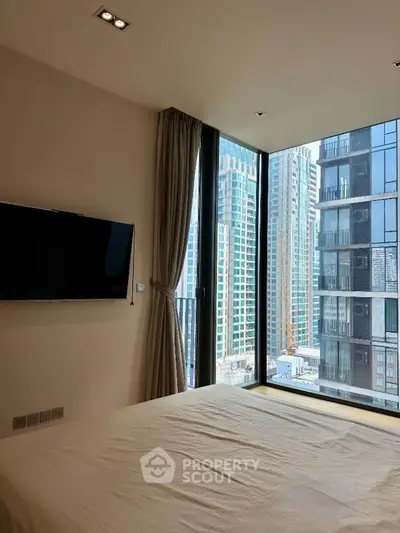 Modern bedroom with large windows offering stunning city views in a high-rise building.