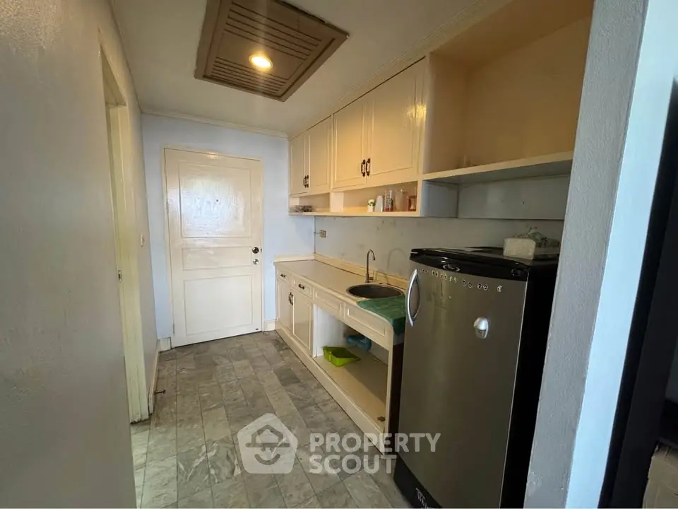 Compact kitchen with stainless steel fridge and marble flooring in cozy apartment.