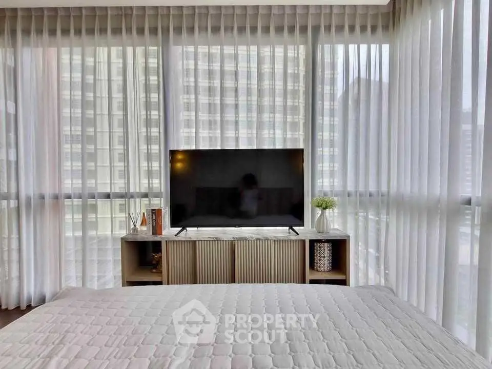 Modern bedroom with large windows and sleek TV setup in urban apartment.
