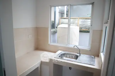 Compact kitchen with a single stainless steel sink and large window offering natural light.