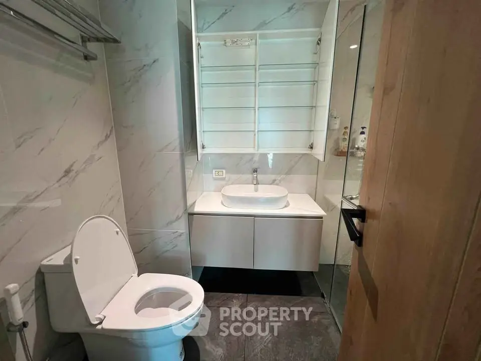 Modern bathroom with sleek design, featuring a white toilet and vanity against marble walls.