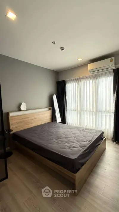 Modern bedroom with large window and wooden flooring in a stylish apartment.