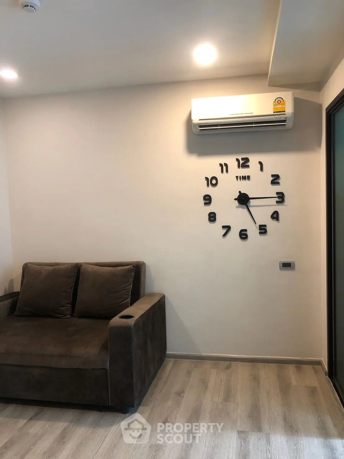 Modern living room with stylish wall clock and cozy sofa, featuring sleek air conditioning unit.