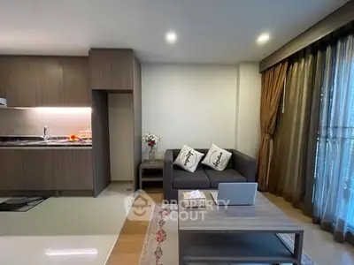 Modern living room with open kitchen, cozy sofa, and natural light from large windows.