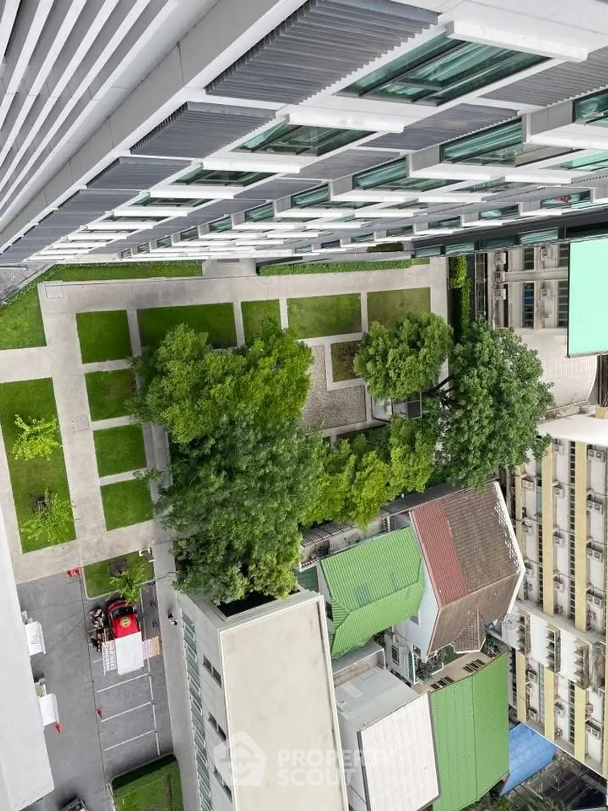 Aerial view of modern apartment building with lush green garden and surrounding urban landscape.