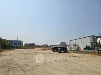 Spacious vacant land with potential for development, featuring clear skies and surrounding buildings.